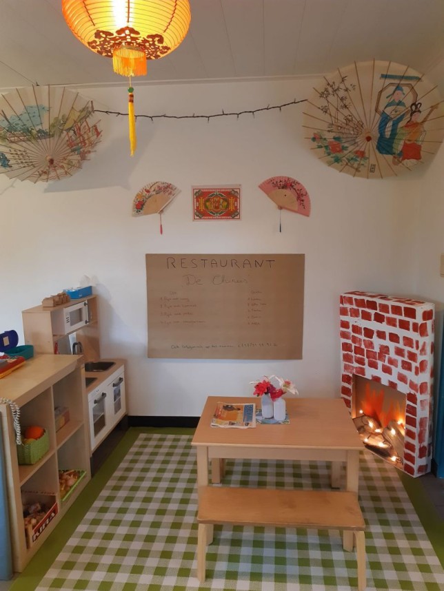Kinderspeelhoek met Chinese decoratie, speelgoedkeuken, houten tafeltje met bankje en nepopen haard.