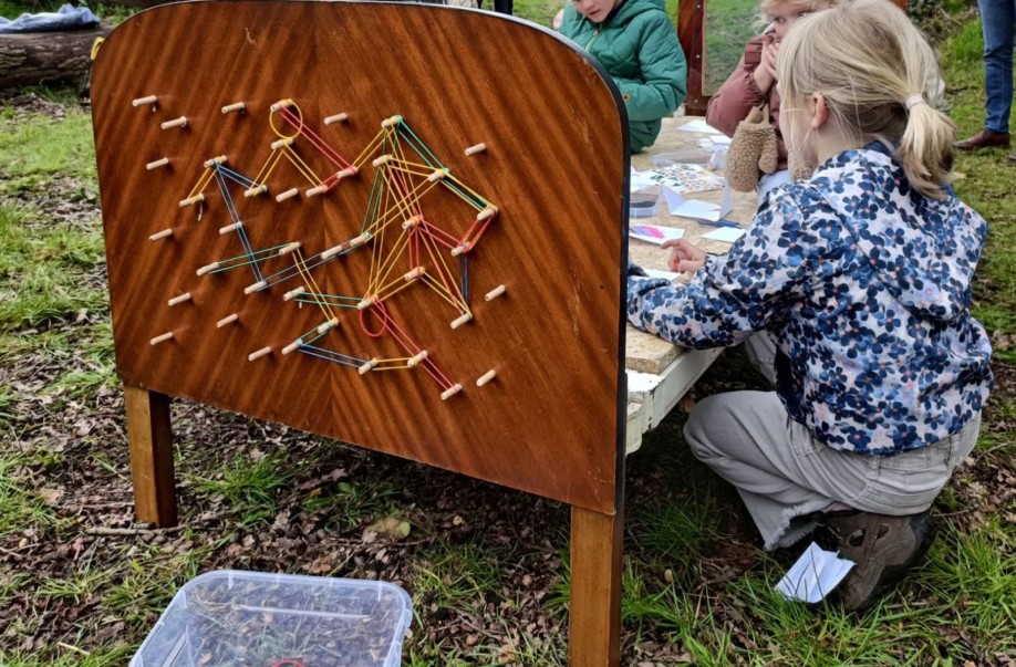 Kinderen knutselen buiten aan een houten bord met kleurrijke elastieken.
