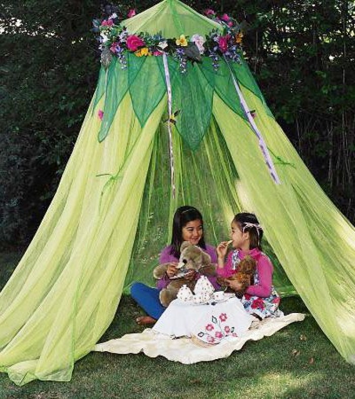 Twee meisjes zitten samen in een groene tent buiten, met knuffels en een theeservies op een kleed.
