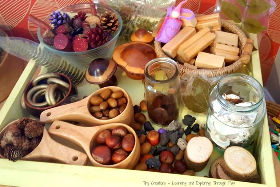 Mandje en houten lepels met kastanjes, eikels, dennenappels, glazen potten en natuurlijke materialen op een tafel.