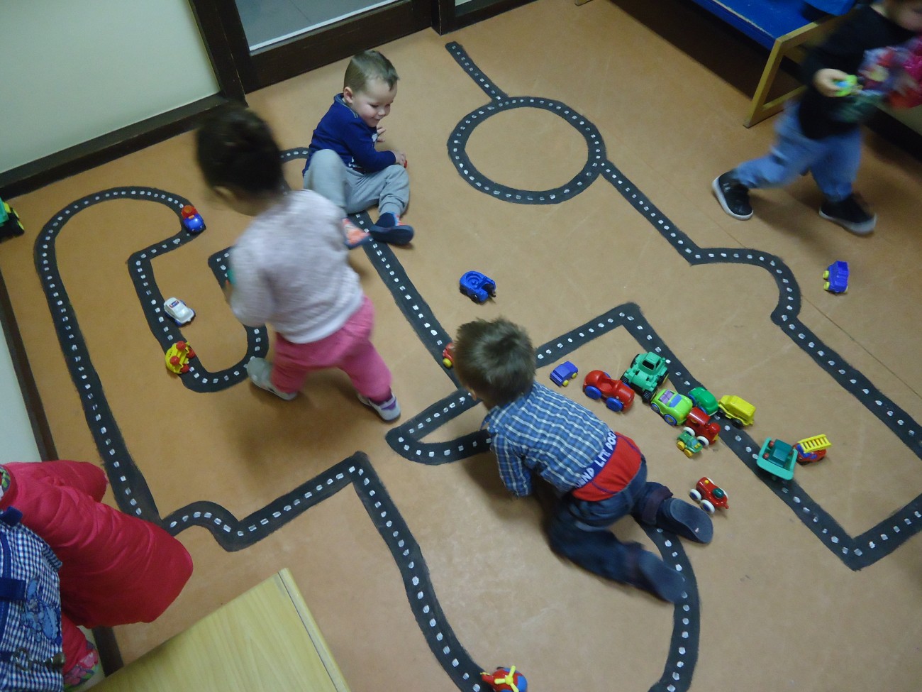Kinderen spelen met speelgoedauto's op een speelvloer met een vlakke weg tekening.