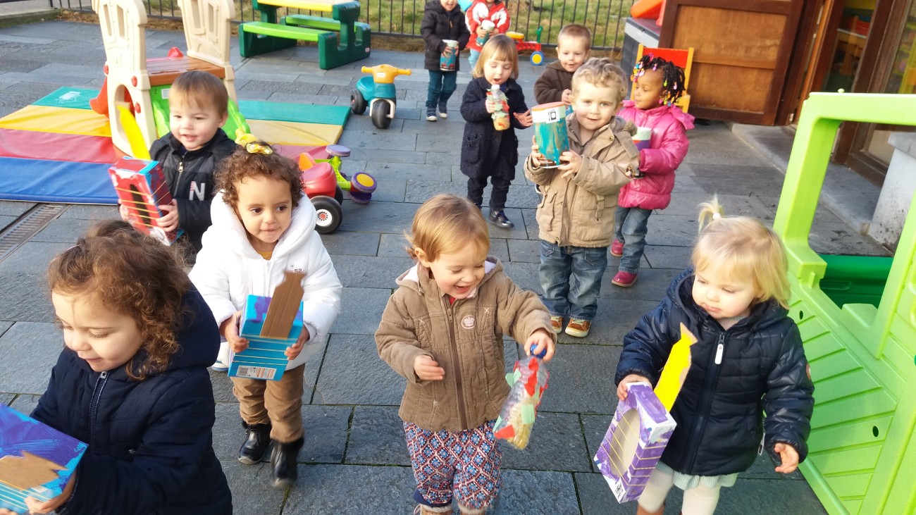 Een groep kinderen loopt met knutselwerkjes in hun handen over een speelterrein.