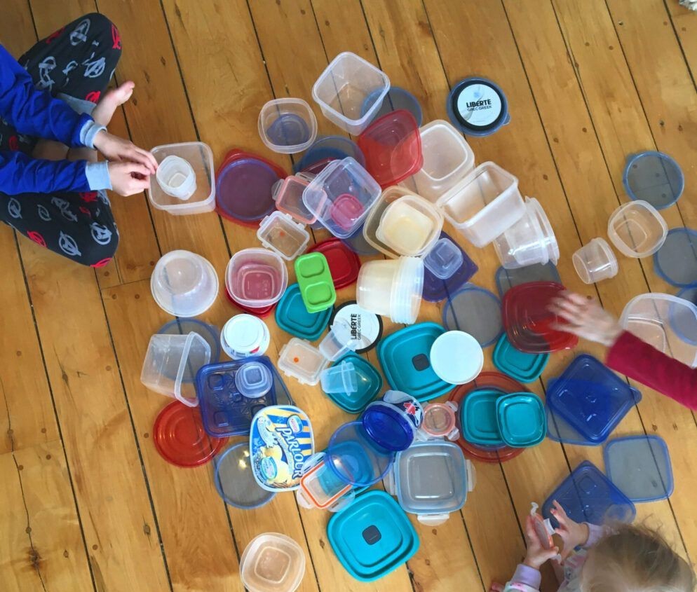 Een kind speelt met kleurige plastic bakjes op een tafel.