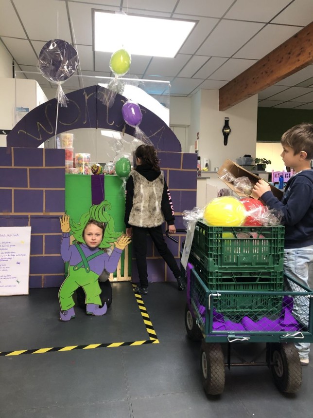 Drie kinderen spelen rond een zelfgemaakt speeltoren met gekleurde ballonnen en speelgoedkastjes binnen.