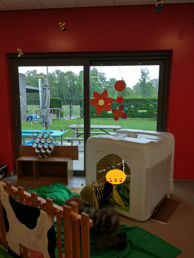 Kinderen spelen binnen in een speelhoek met raam naar buiten en decoraties aan het raam.