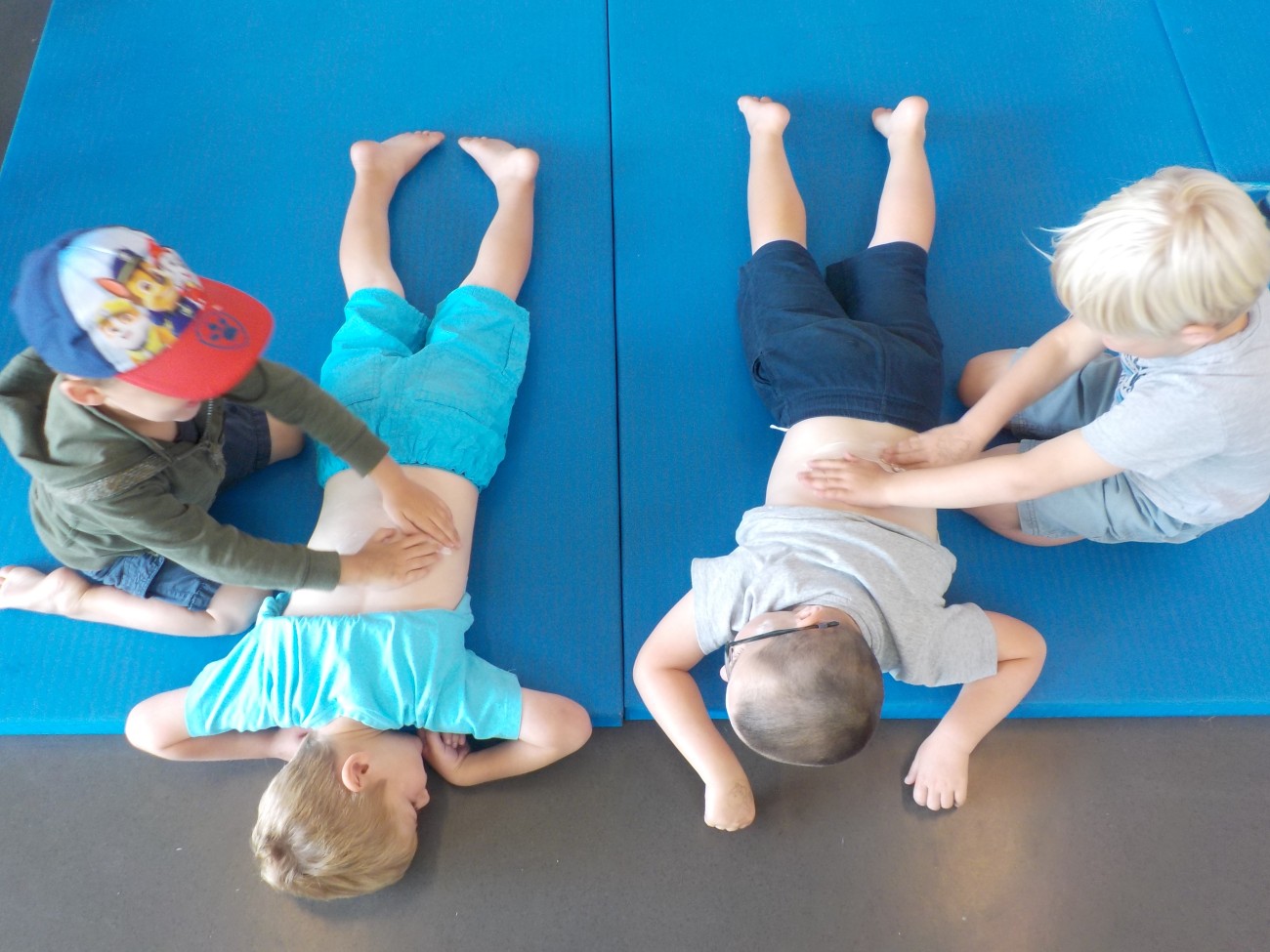 Vier kinderen liggen op blauwe matten en geven elkaar een rugmassage.