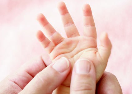 Een hand van een jong kind wordt vastgehouden door een volwassene, met een zachte, roze achtergrond.