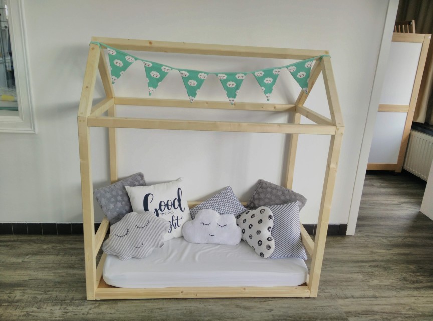 Houten kinderbed in de vorm van een huisje met witte matras, kussens en een groene vlaggenlijn.