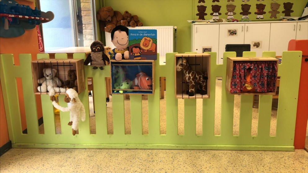 Groene speelpoort met verschillende knuffels en kleine kamertjes in een kleuterschoolklasje.