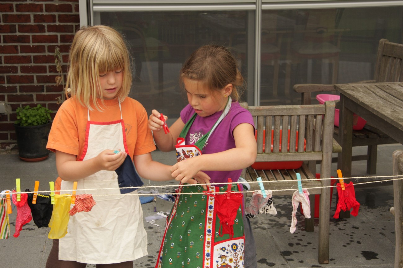Twee kinderen hangen was aan een lijn buiten, met kleurige kleertjes en een houten tafel op de achtergrond.