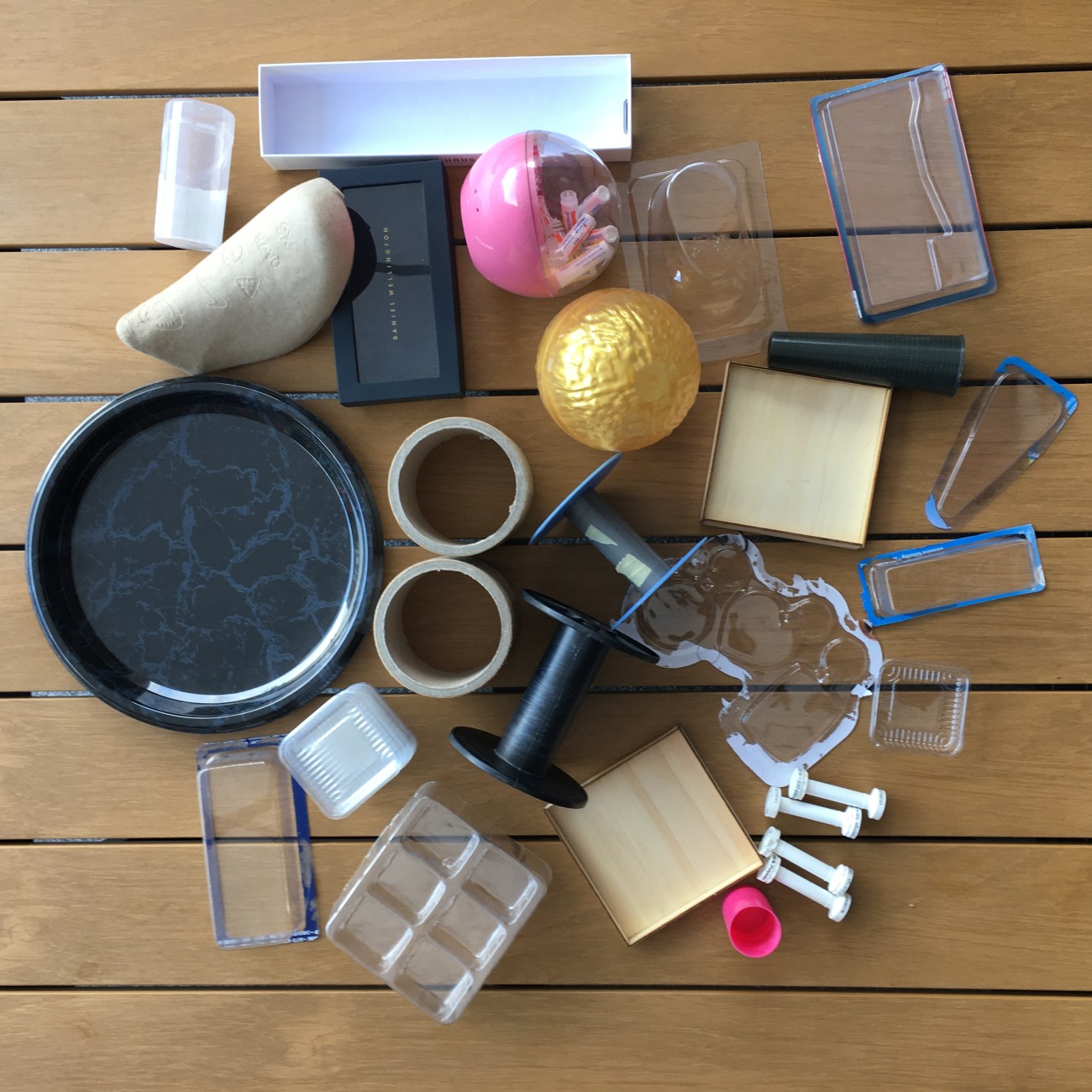 Een verzameling objecten waaronder doosjes, een gouden bal, tape en een schaal op een houten tafel.