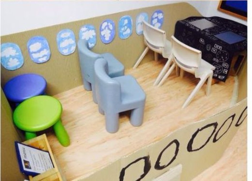 Speelhoek voor kinderen met kleine stoelen, een tafeltje en blauwe wolkenstickers op de muur.