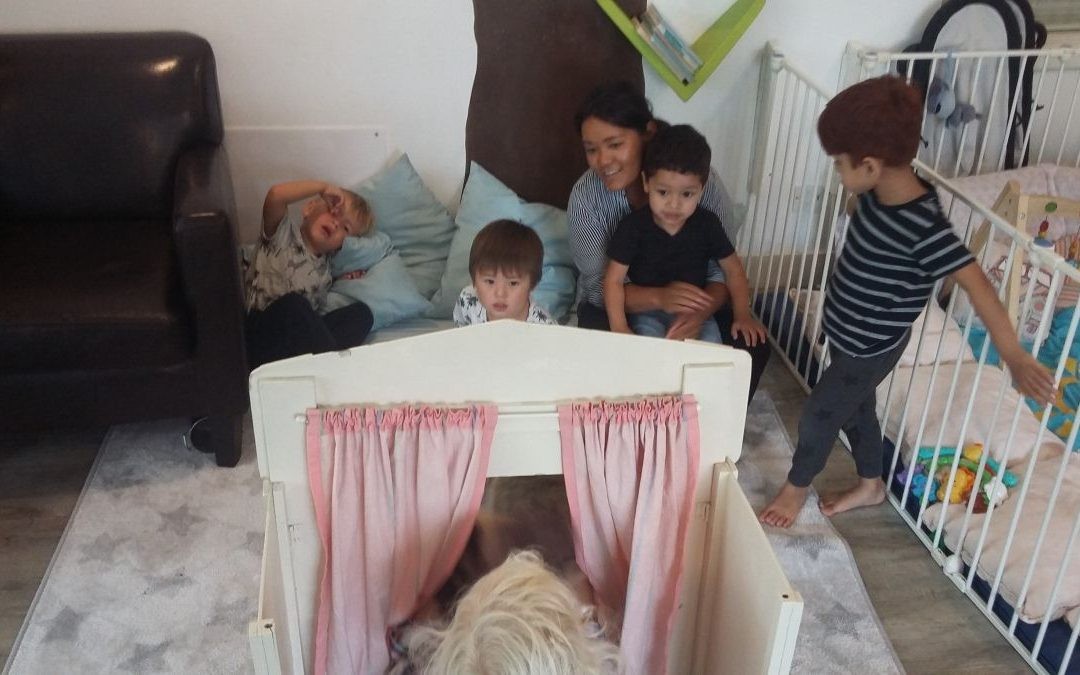 Een vrouw met vier kinderen kijkt naar een kleine show achter een houten poppentheater.
