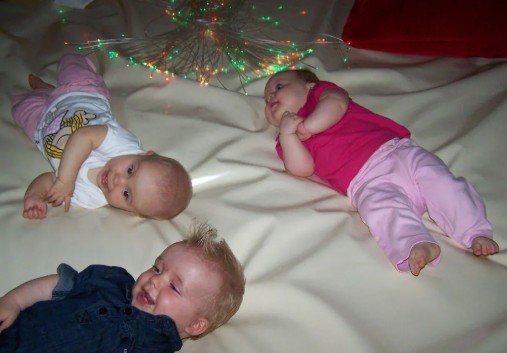 Drie baby's liggen op een zachte ondergrond onder kleurrijke lichtjes.
