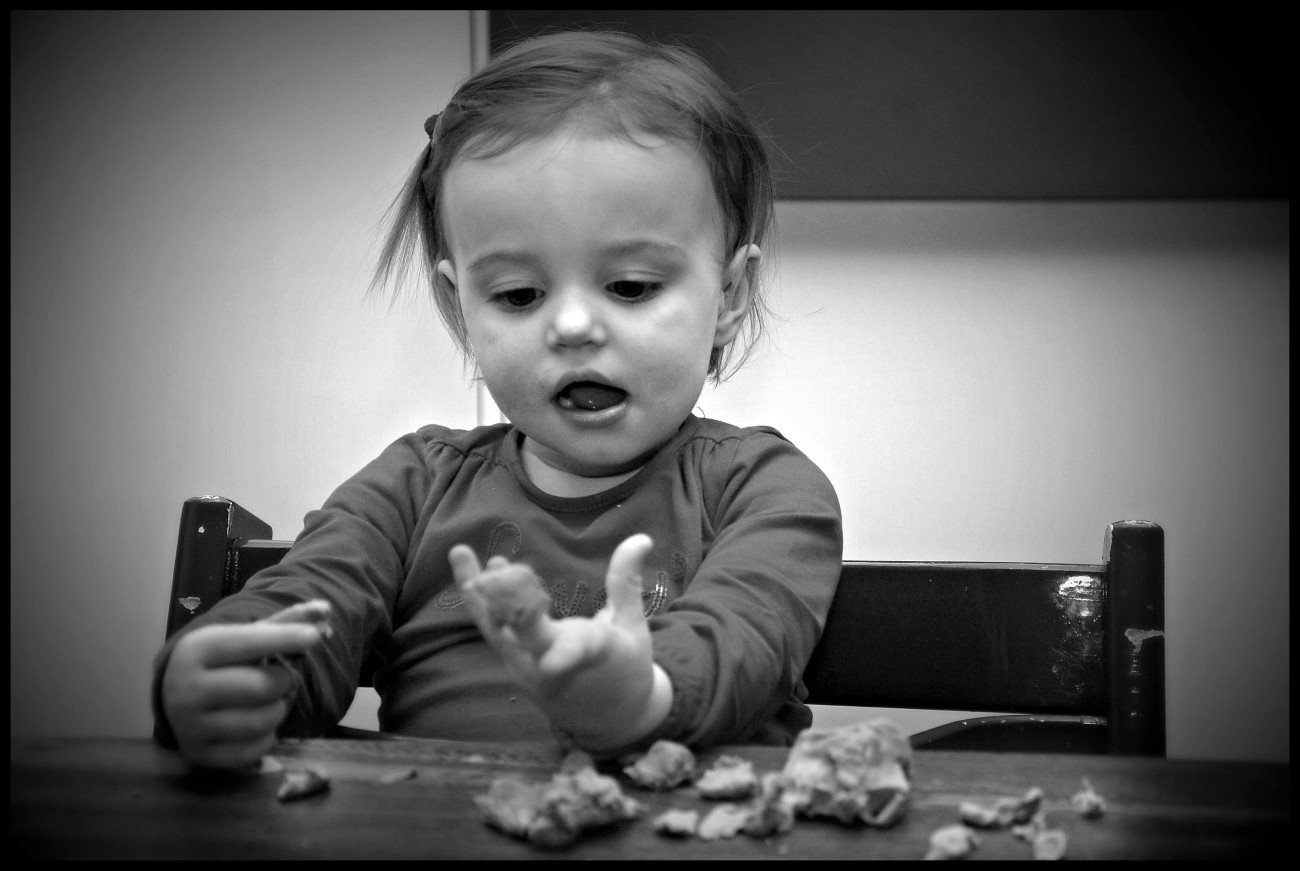 Een peuter zit aan een tafel en speelt met stukjes voedsel.