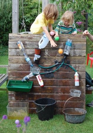 Twee kinderen spelen met een houten waterbaan, waarbij ballen en flessen van verschillende materialen worden gebruikt.